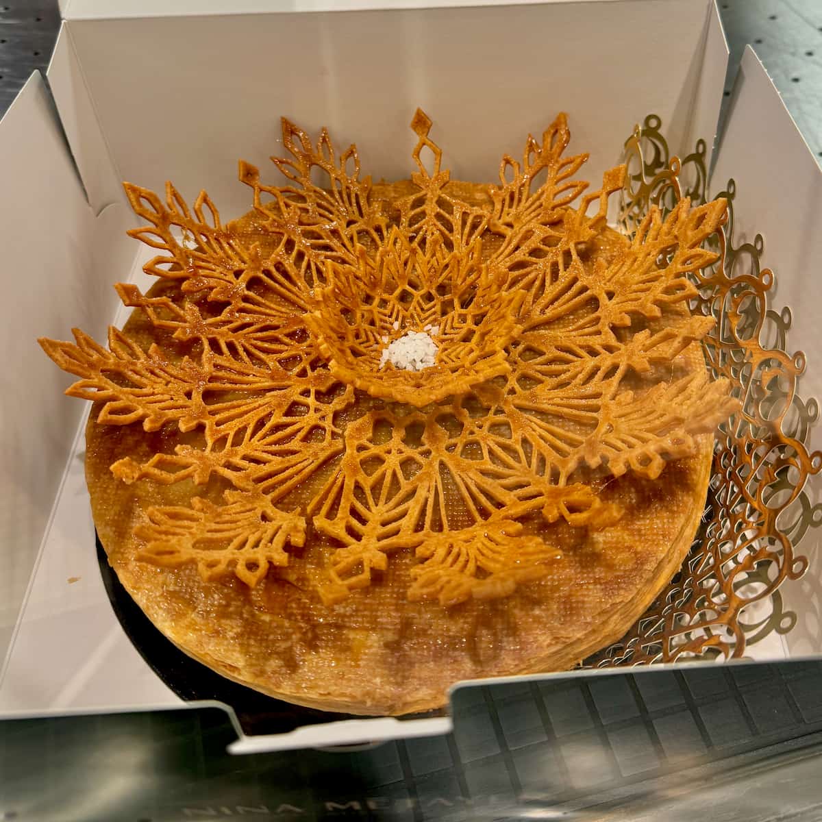 box of an ornate puff pastry cake with a lace like topping