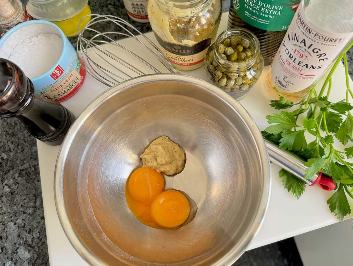 bowl of 2 egg yolks and mustard with rest of the recipe ingredients as a mise en place.