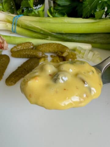 spoonful of homemade Tartar sauce with gherkins, onion and caper ingredients in background
