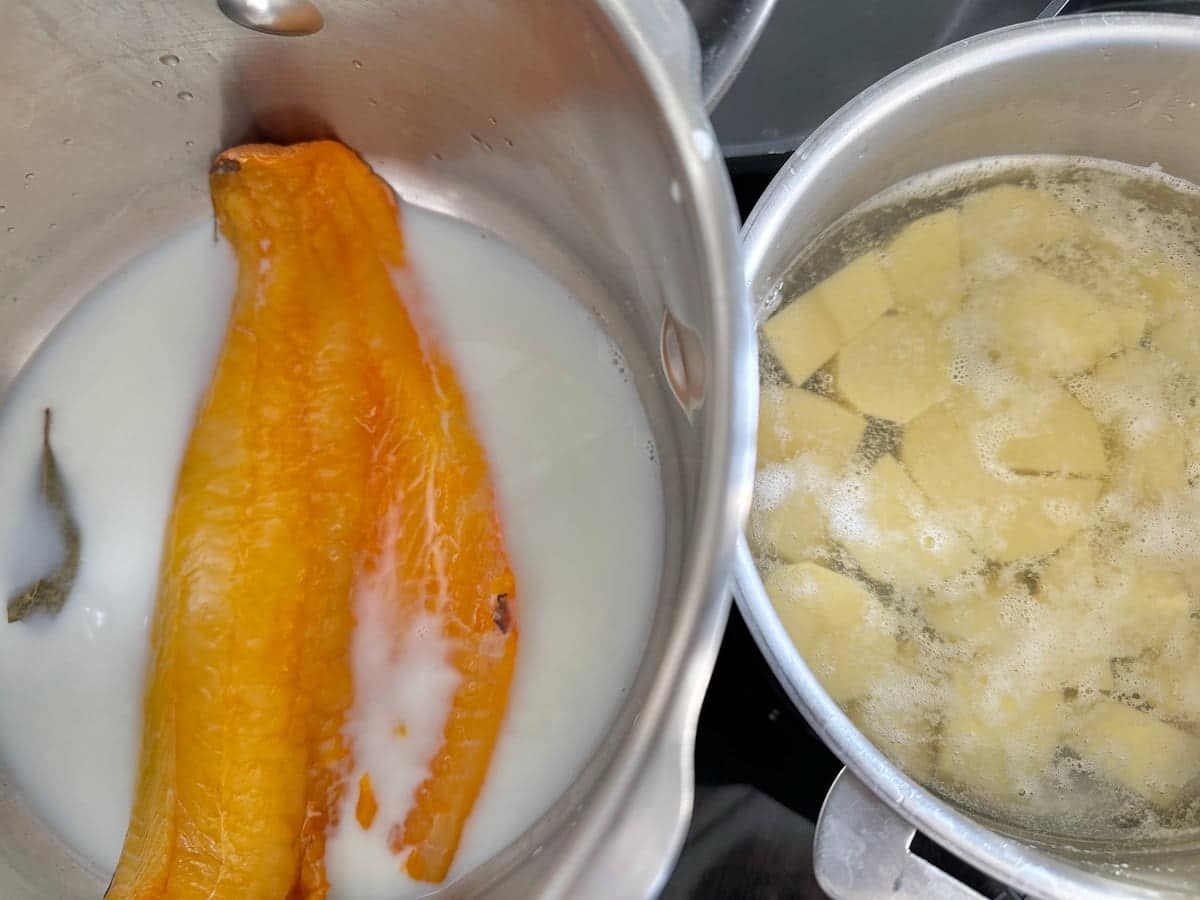 a large pan poaching smoked haddock and another one cooking potatoes in boiling water