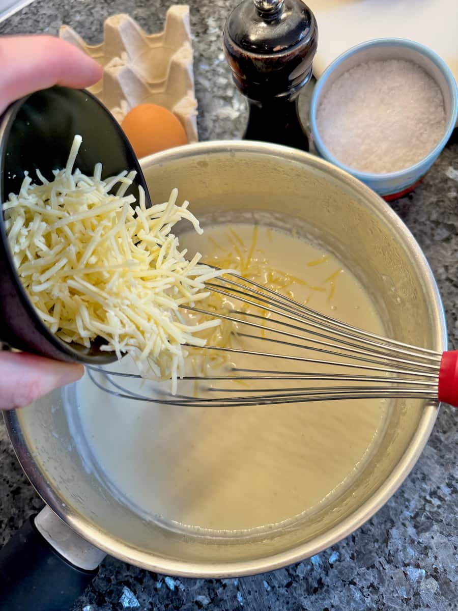adding grated French emmental cheese to bechamel sauce 