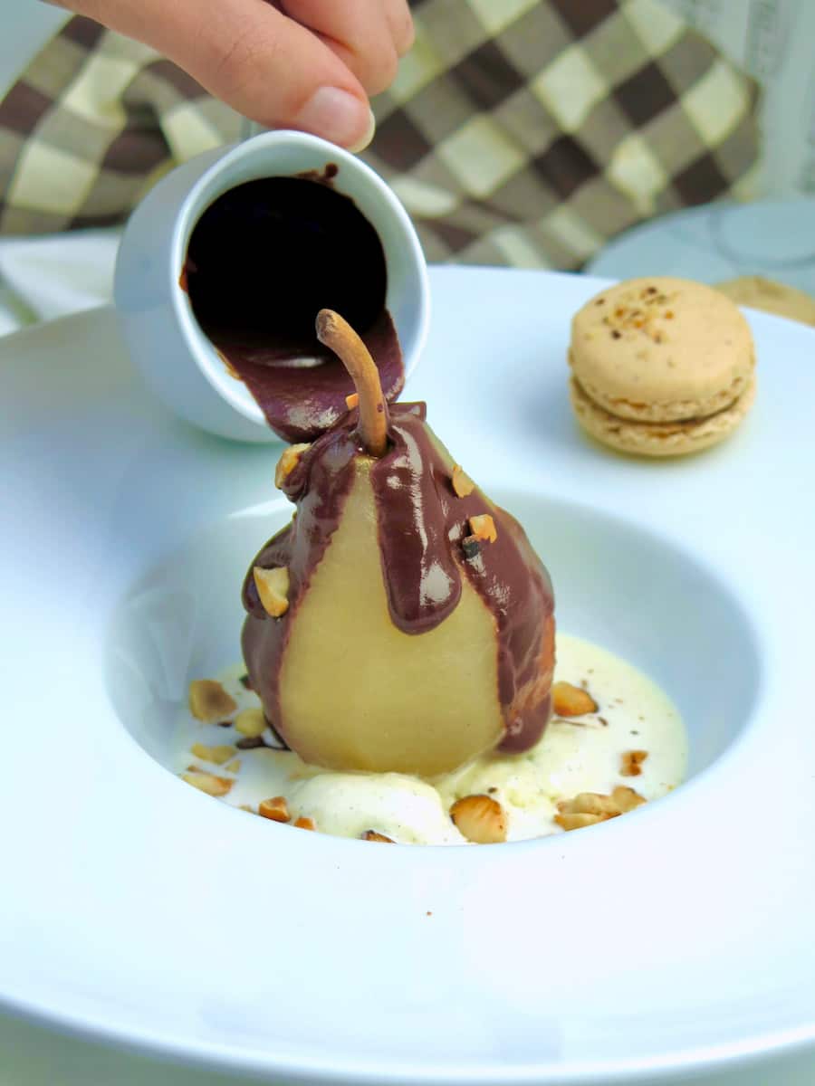 pouring thick dark chocolate sauce onto a poached pear and ice cream to make a poire belle helene dessert