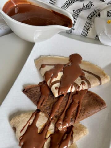 pouring dark chocolate sauce over crepes