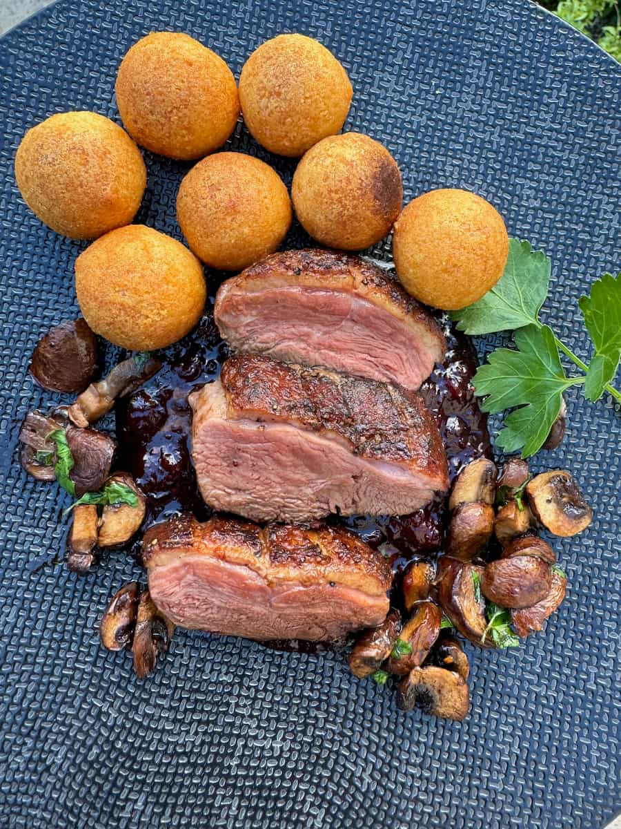 plate of 3 seared pink duck breast slices on top of a cherry sauce, mushrooms and Dauphine potatoes