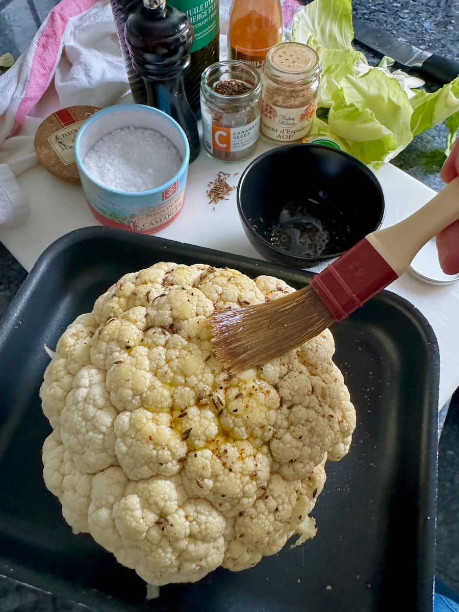 Using a pastry brush to coat a cauliflower with olive oil and seasoning