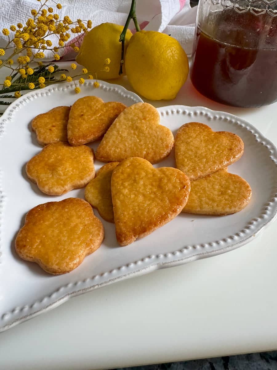 plate of glazed heart and flower shaped cookies with a pot of honey and 2 lemons