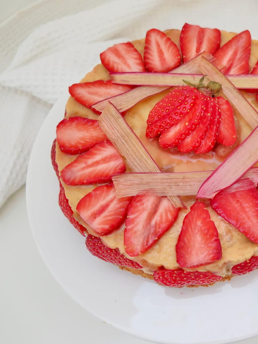 close up of a vanilla cheesecake topped with sliced strawberries and dried rhubarb chips