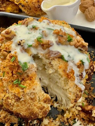 whole roasted cauliflower, showing a tender interior topped with a cheese crust and sauce
