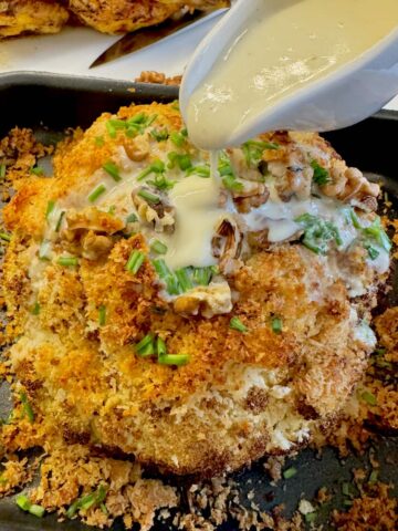 pouring cheese sauce over a whole roasted cauliflower topped with crispy cheese and walnuts