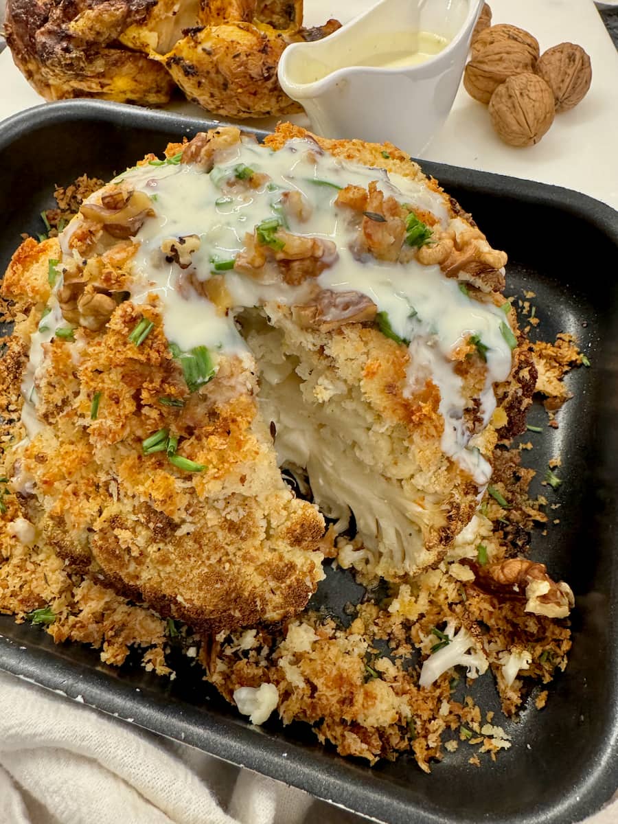 whole roasted cauliflower sliced open to reveal tender vegetable, covered in a cheese crust and sauce