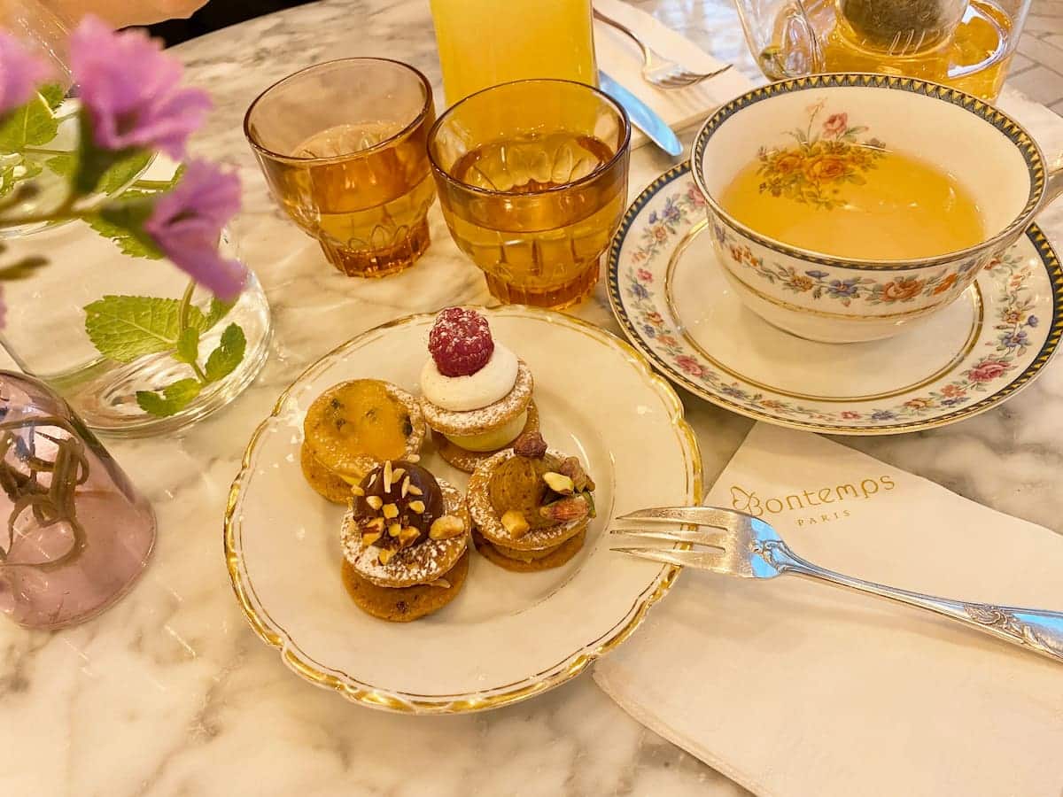 mini cakes on a plate next to tea in a china cup with flowers