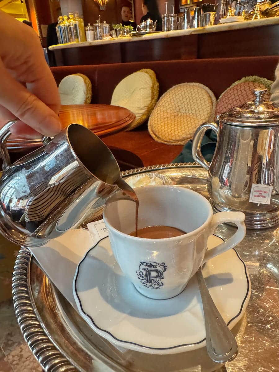 pouring a silver jug of chocolat chaud into a porcelain cup at le Procope Paris