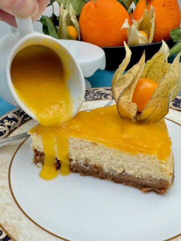 pouring a jug of fresh mango sauce over a slice of cheesecake