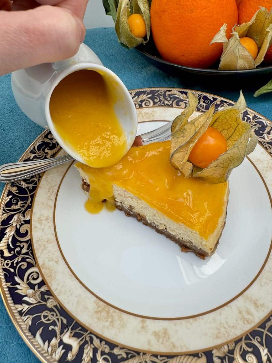 pouring mango sauce from a pot over a creamy orange dessert