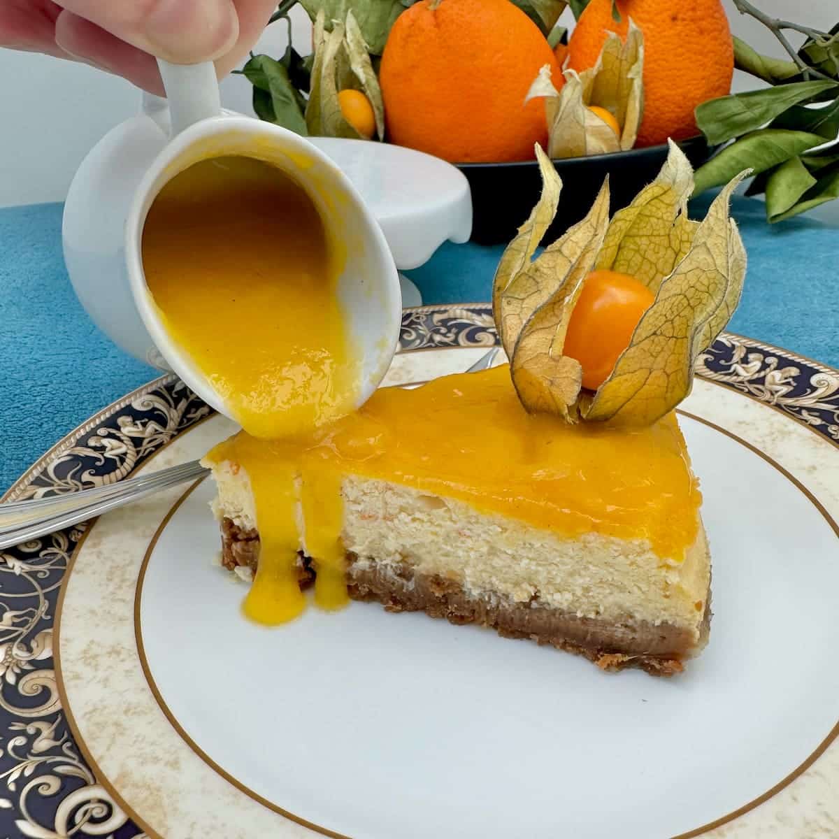 pouring a jug of fresh mango sauce over a slice of cheesecake