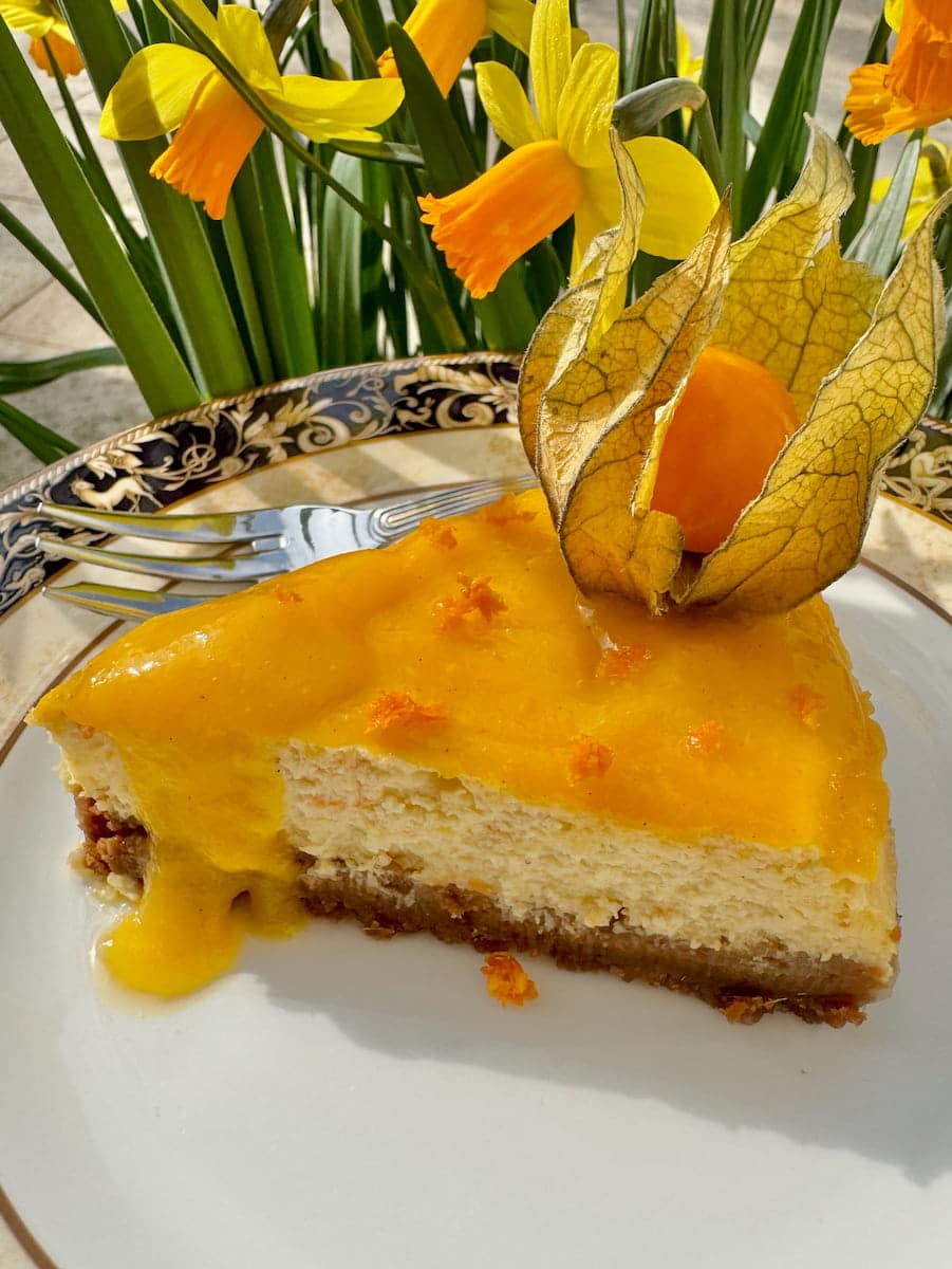 slice of orange cheesecake topped with mango coulis and a cape gooseberry