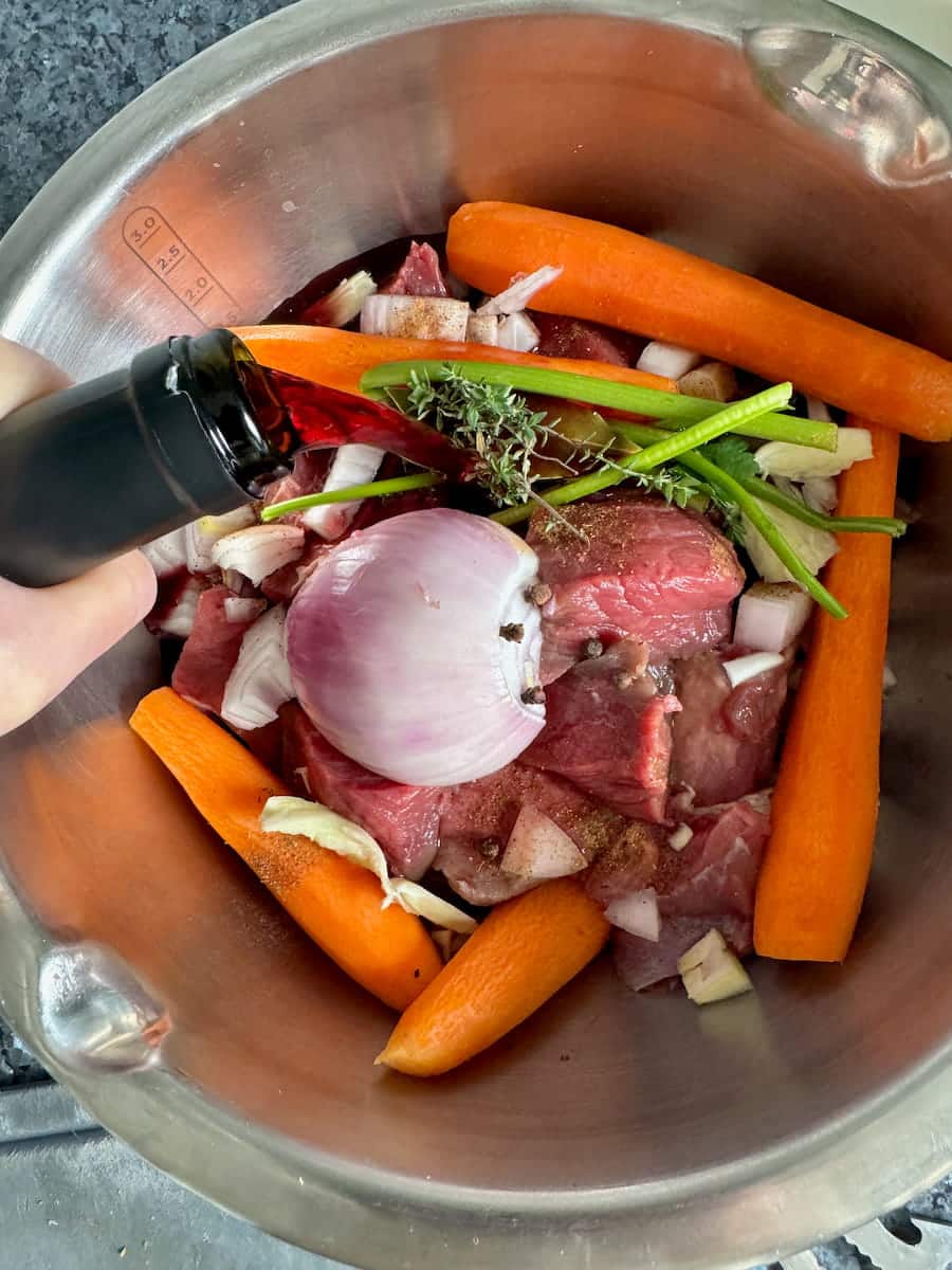 pouring red wine into a marinade of beef, carrot, garlic, onion and spices