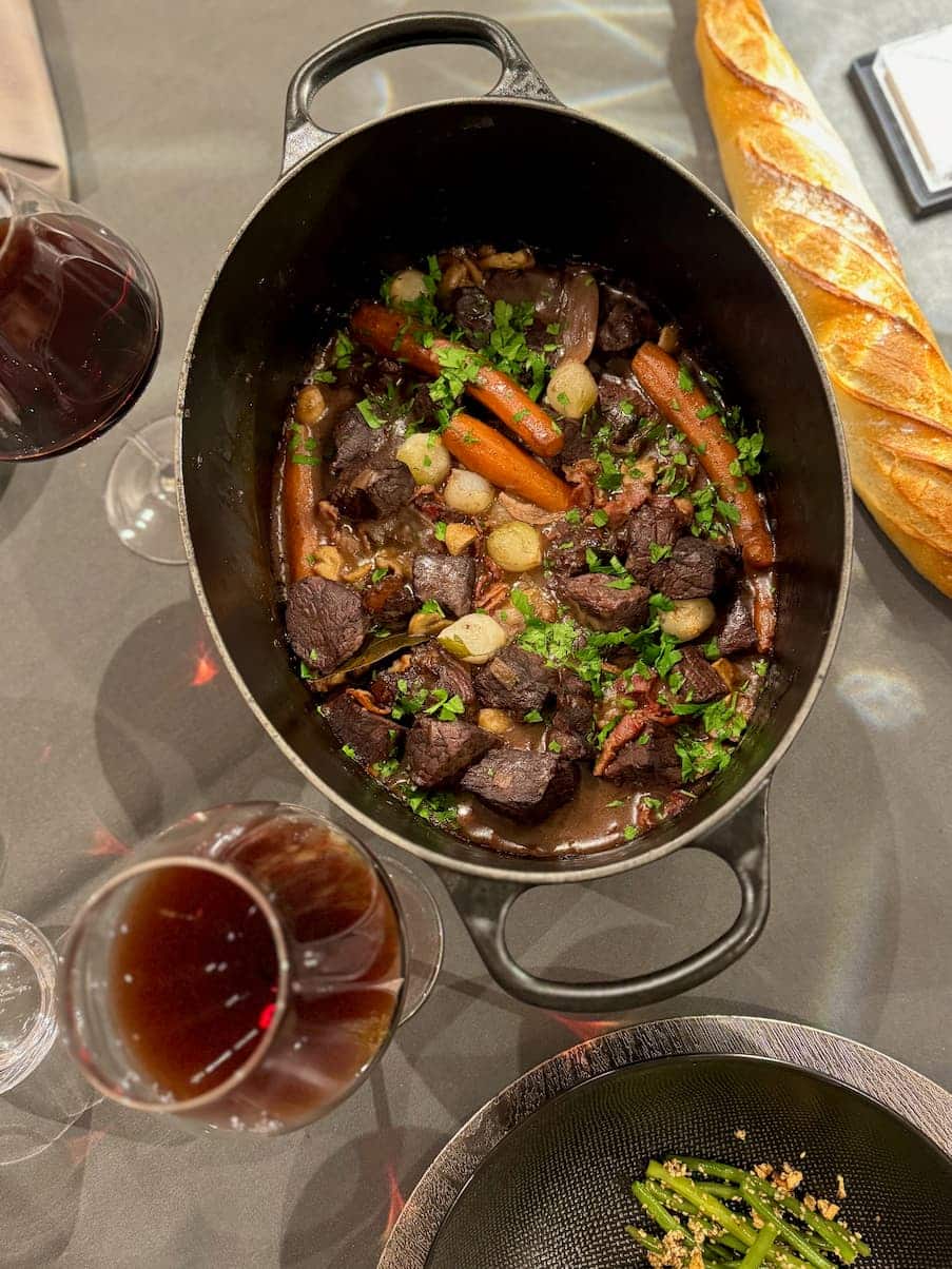 crock pot of French beef stew served with green beens, a baguette and red wine