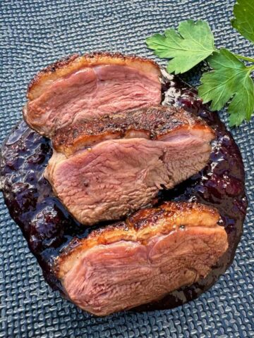 plate of 3 seared pink duck breast slices on top of a cherry sauce