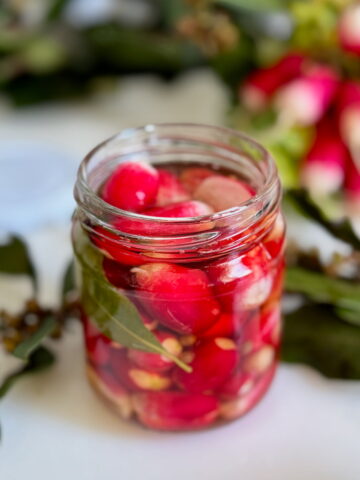 jar of bright pink pickled radishes with bay leaves