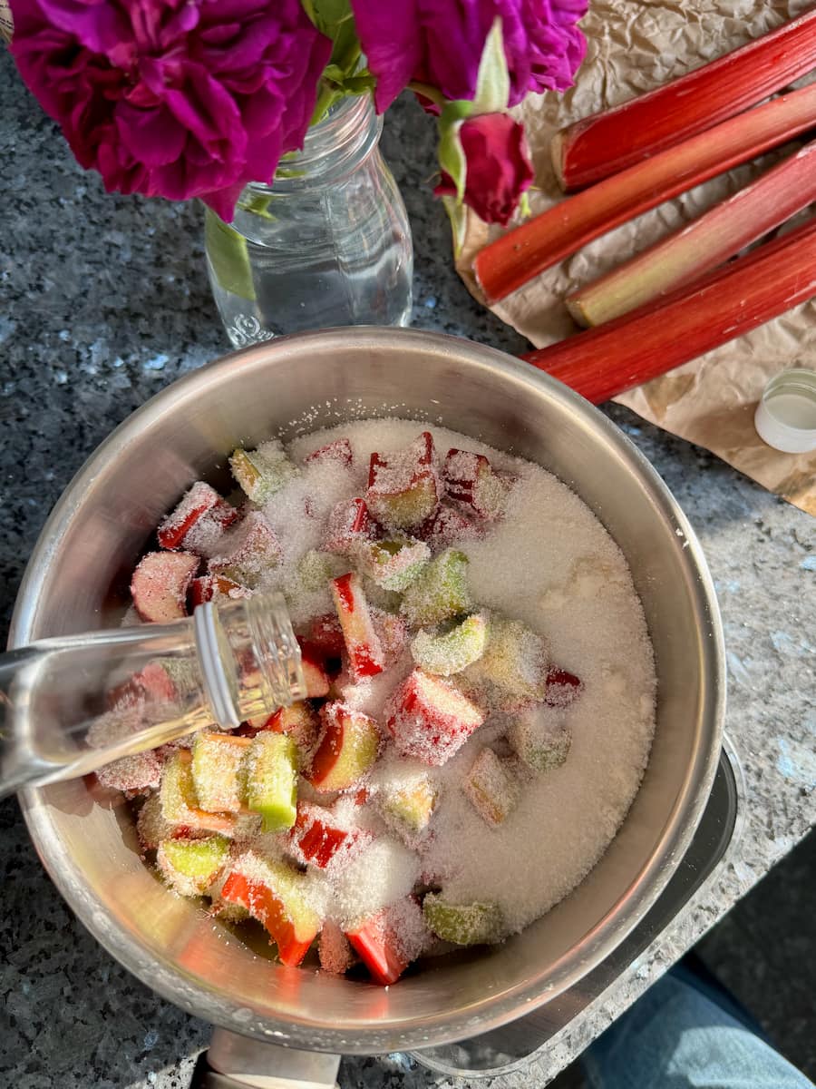 pouring a little rosewater into a pan of rhubarb and sugar