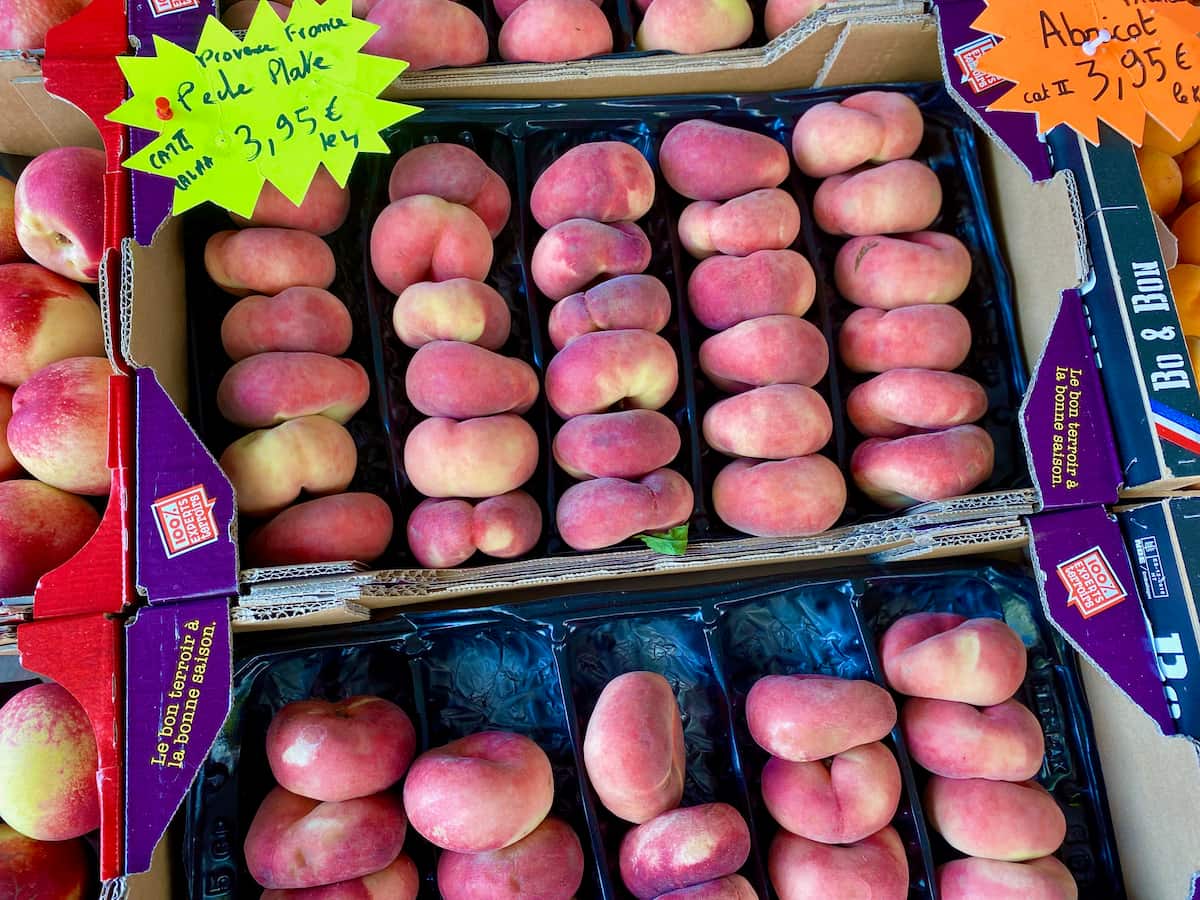 crates of flat peaches at a French market, with a sign saying peches plate