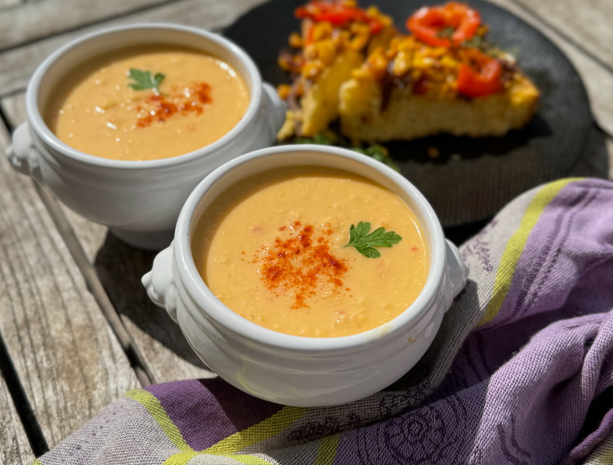 two French lion soup bowls with sweetcorn chowder topped with paprika next to cornbread