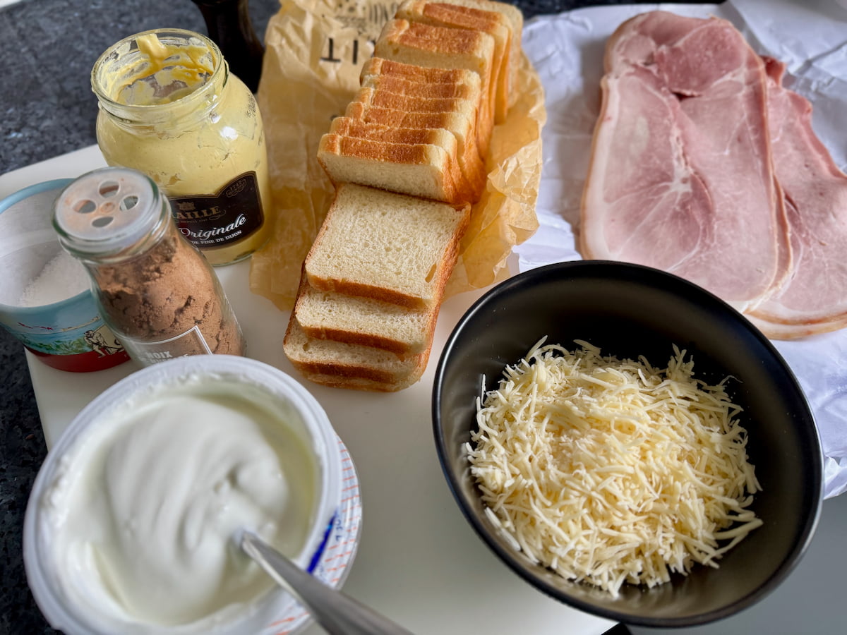 ingredients laid out to make a croque monsieur - French sandwich bread, Parisian ham slices, grated Emmental cheese, creme fraiche, mustard, nutmeg, salt and pepper