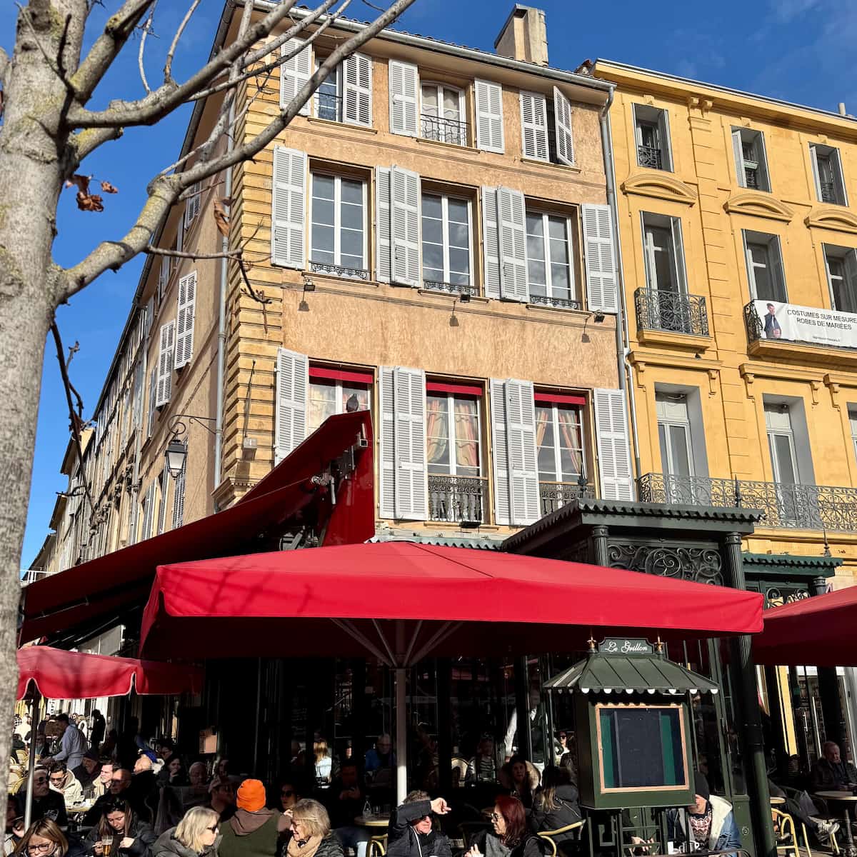 bustling café in Aix-en-Provence in the sunshine with people drinking coffee outside next to a plane tree