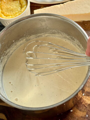 whisking a hot parmesan cream sauce in a saucepan next to a block of Parmigiano Reggiano cheese