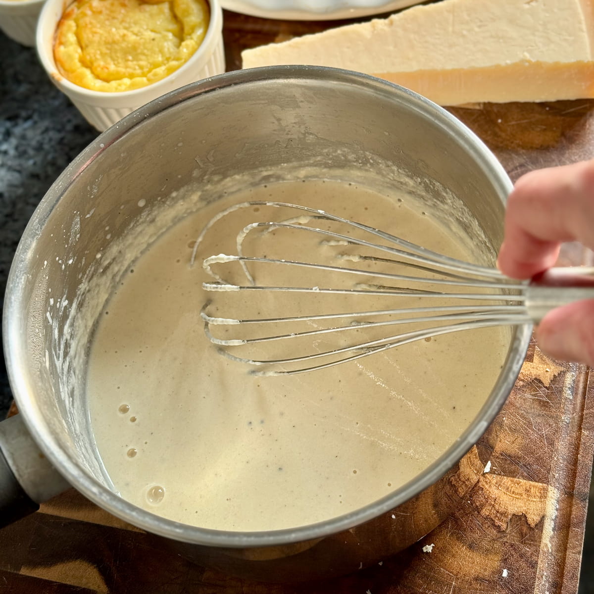 whisking a hot parmesan cream sauce in a saucepan next to a block of Parmigiano Reggiano cheese