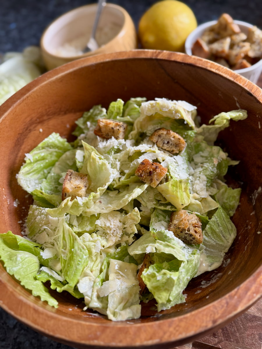 large salad bowl with romaine lettuce tossed in Caesar dressing and topped with grated parmesan and crispy garlic croutons