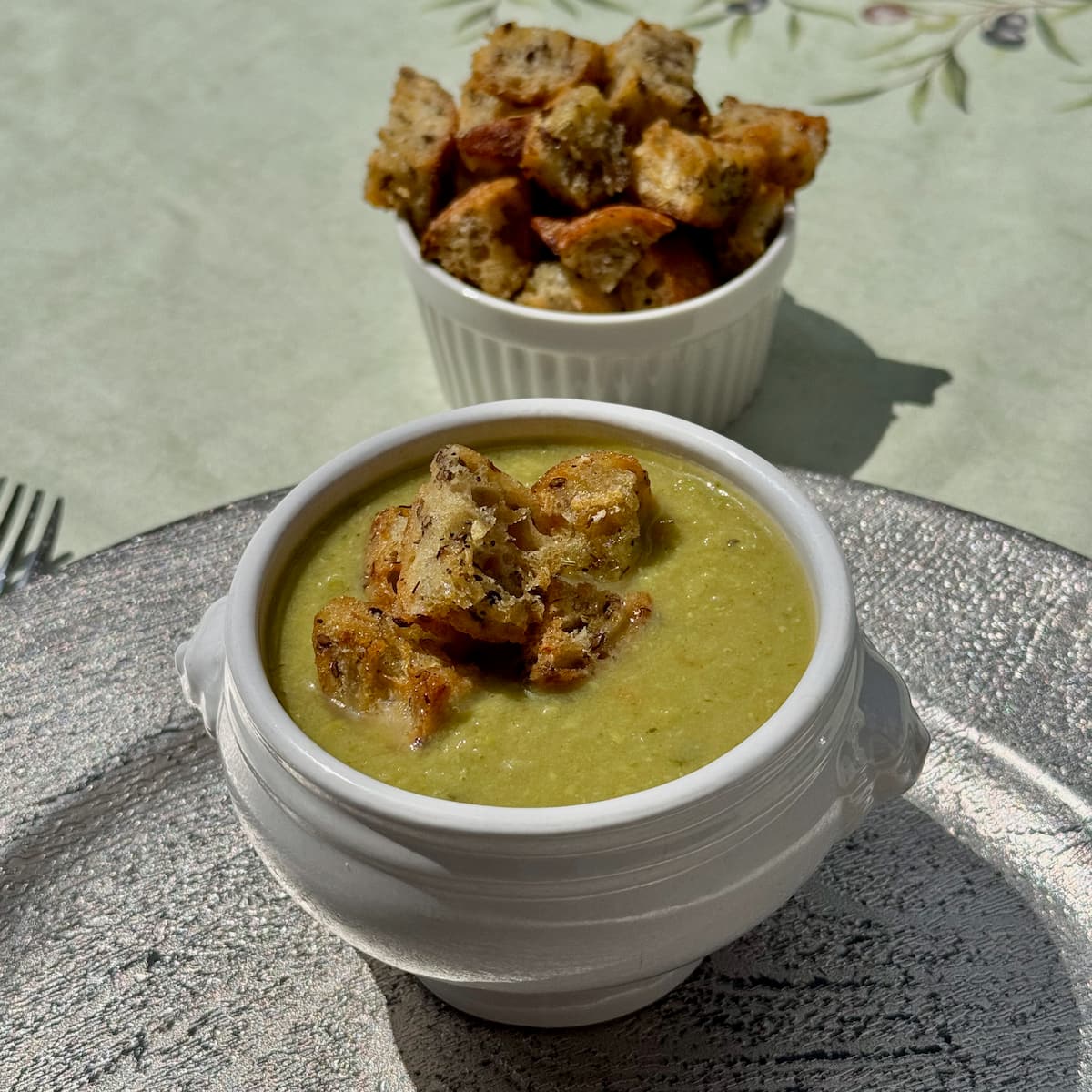 homemade croutons made with garlic and French bread topping for a pea soup next to a ramekin of more croutons
