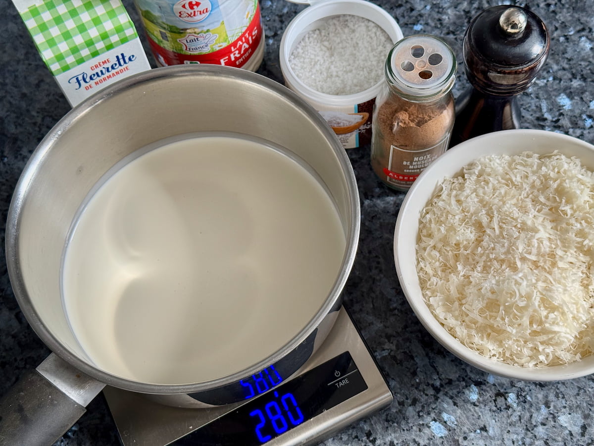ingredients laid out to make a parmesan cream sauce with heavy cream, whole milk, grated Parmiggiano Reggiano, nutmeg, pepper and salt