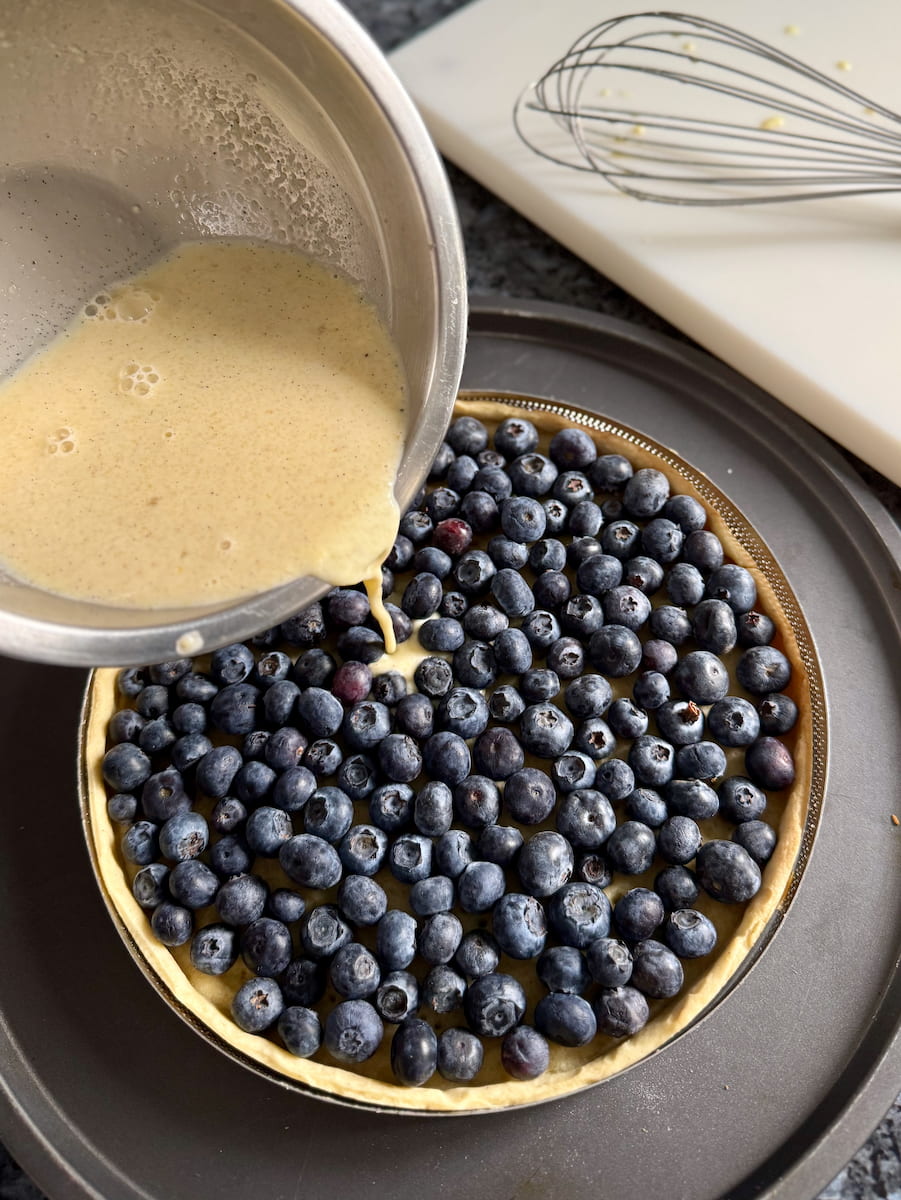 pouring a quick custard filling over fresh blueberries and a sweet pastry crust