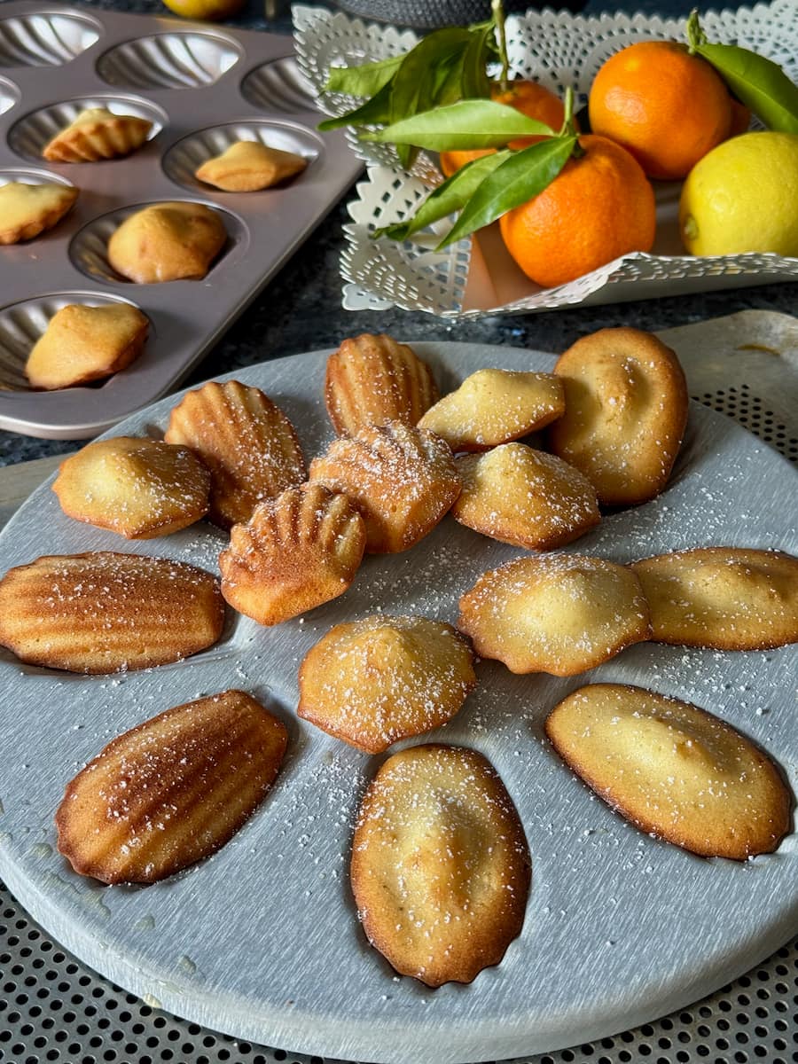 baked madeleine cakes showing a raised hump in the middle, being removed from their tins