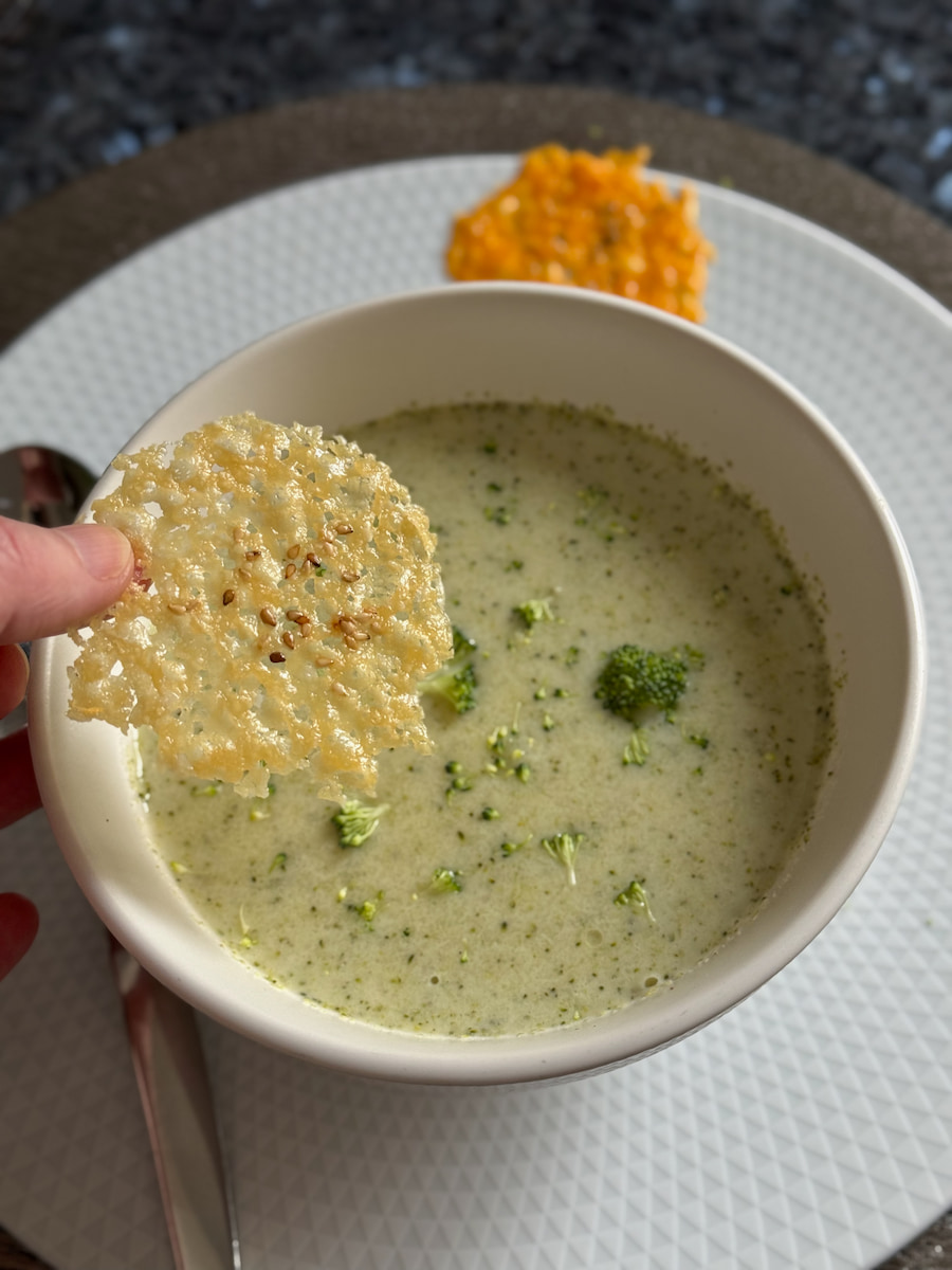 a large bowl of creamy broccoli soup holding a Parmesan crisp that looks like lace