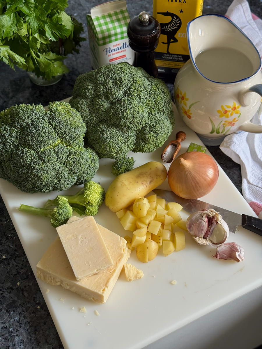 ingredients laid out to make a creamy broccoli cheese soup - with white cheddar, potato, onion, garlic, stock, cream and broccoli.