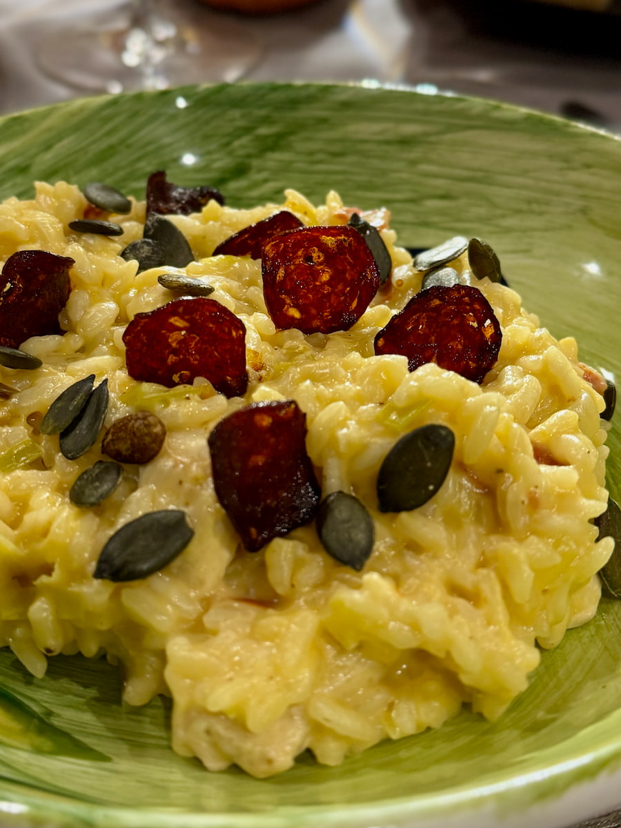 bowl of creamy risotto garnished with thin chorizo crisps and toasted pumpkin seeds