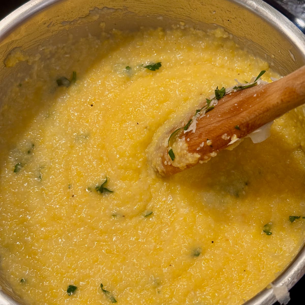 stirring a creamy corn polenta with a wooden spoon to incorporate cheese and butter