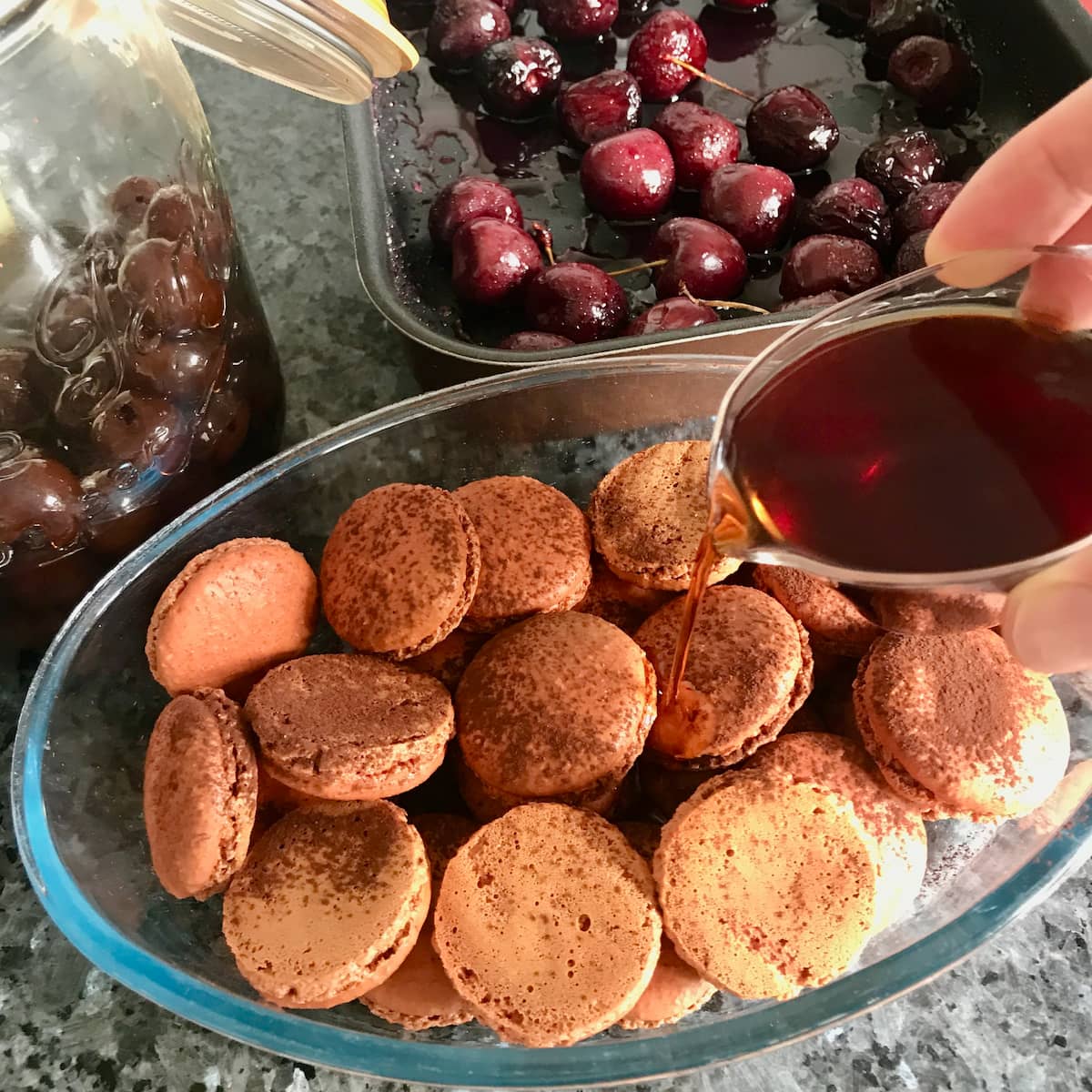 pouring syrup over cracked macaron shells with roasted cherries to make a dessert