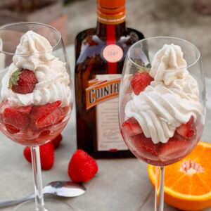 large wine glasses with marinated strawberries in orange liqueur and orange topped with vanilla Chantilly cream