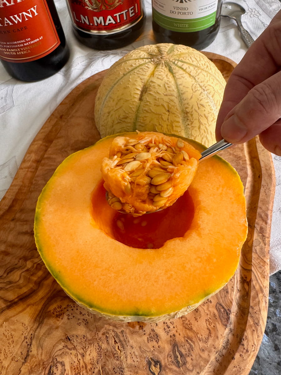 scooping out the seeds from the middle of an orange Cantaloupe melon - the ideal cavity to fill with Port