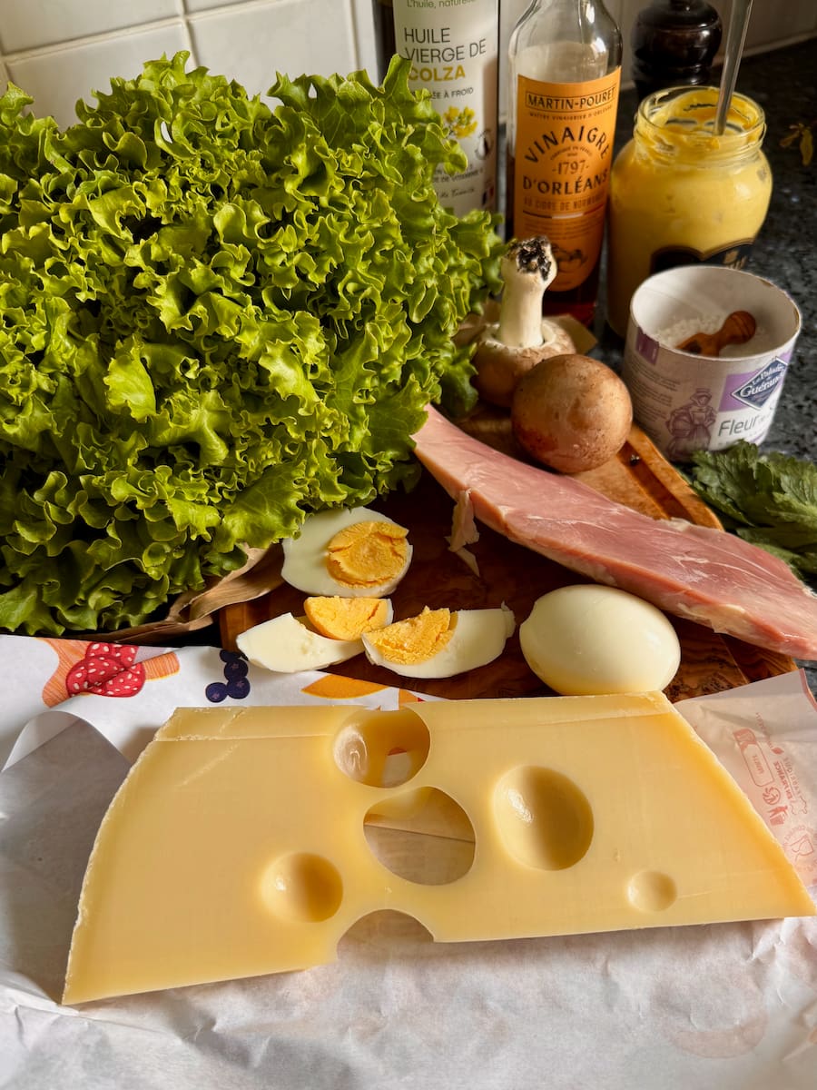 ingredients laid out to prepare a Parisian salad: Emmental cheese, hard boiled egg, good hunk of cooked ham, batavia curly lettuce and mushrooms with vinaigrette