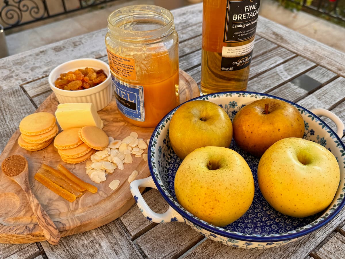 Ingredients for French baked apples, including whole apples, honey, cinnamon and dried fruit.