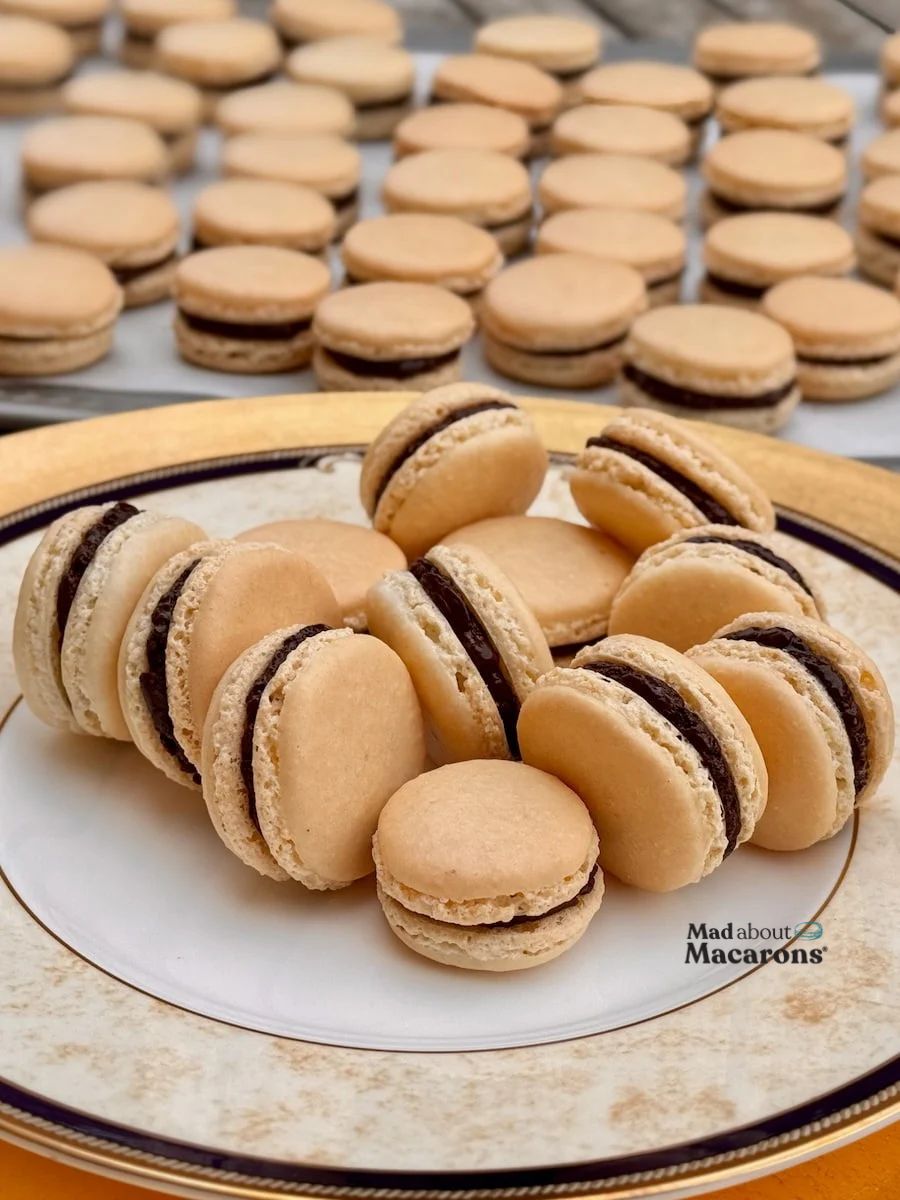 plate of plain French macarons with pretty feet, filled with dark chocolate on a golden plate