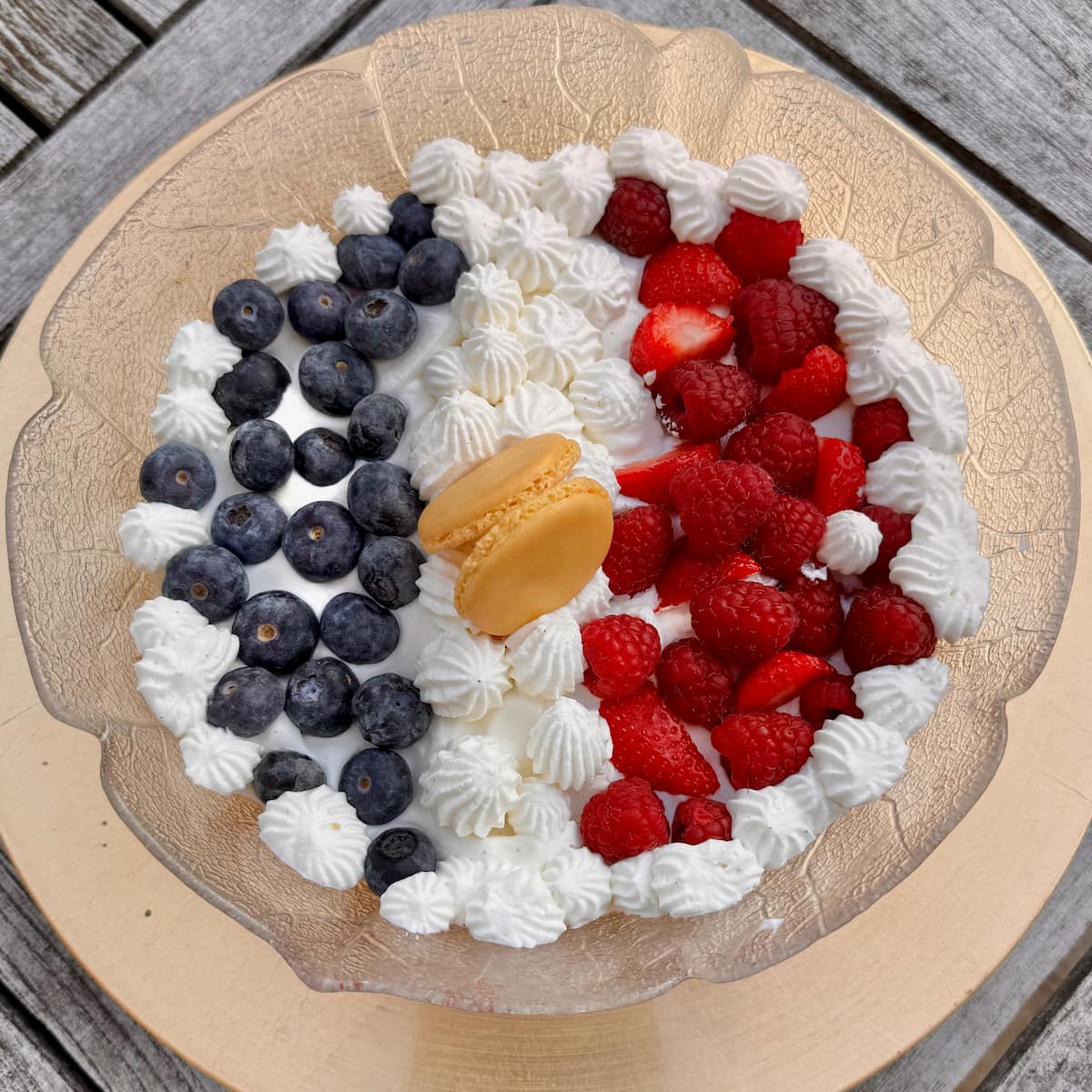 large trifle bowl made with macarons and topped with fresh vanilla cream, blueberries, raspberries and strawberries and decorated with macaron shells